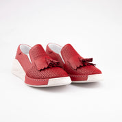 A USA studio shot showcasing the MrCalvano Newport Beach women's slip-on comfort shoes in vibrant red leather. The image highlights the detailed geometric perforations on the vamp, the decorative leather tassels, and the distinct white wedge sole. The shoe's profile suggests ease of wear and ergonomic support, characteristic of a casual yet refined style.