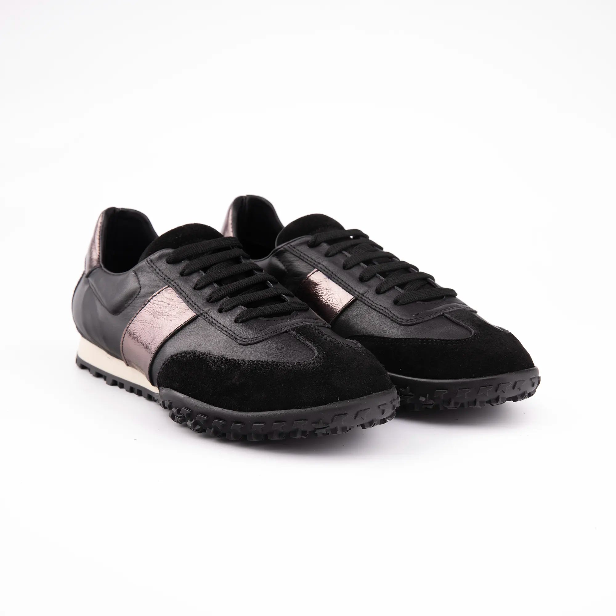 A close-up view of the MrCalvano Pebble Beach black leather women's shoes, showcasing the contrasting textures of smooth leather, suede details, and the subtle metallic rose-gold accent stripe. The well-defined lug pattern on the black sole is visible, emphasizing the shoe's urban-ready construction.
