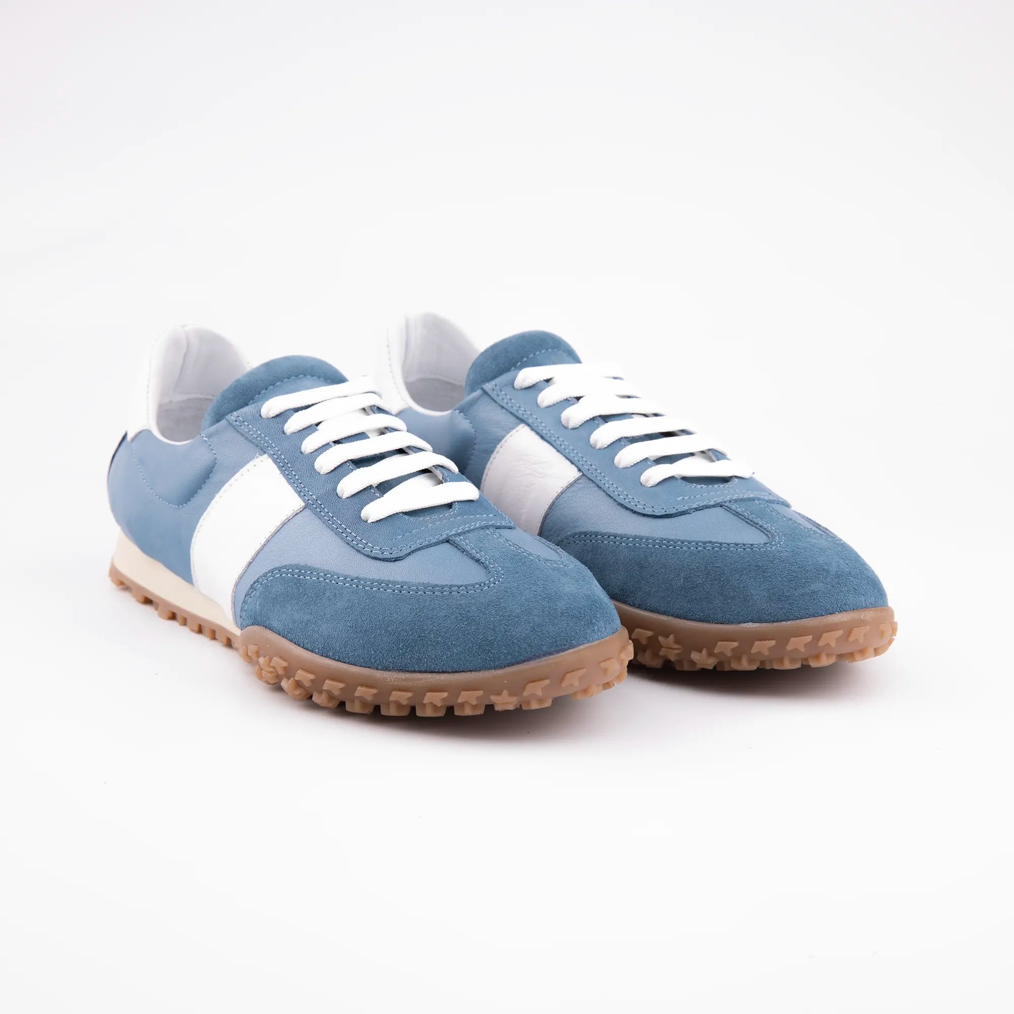 A United State studio shot highlighting the texture and color of the blue leather upper, white detailing, and gum sole of the Pebble Beach women's sneakers, emphasizing material quality.