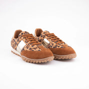A clean studio shot of the MrCalvano Pebble Beach women's sneakers, showcasing the leopard print leather, gold metallic accents, and brown suede details. The neutral rubber sole and brown laces are visible, highlighting the product's distinctive design and material mix.
