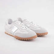 A detailed California studio shot highlighting the texture of the full-grain white leather, the softness of the light grey suede, and the subtle shimmer of the metallic silver side stripes on the MrCalvano Pebble Beach women's sneakers. The gum sole's unique tread is visible, emphasizing functional design.