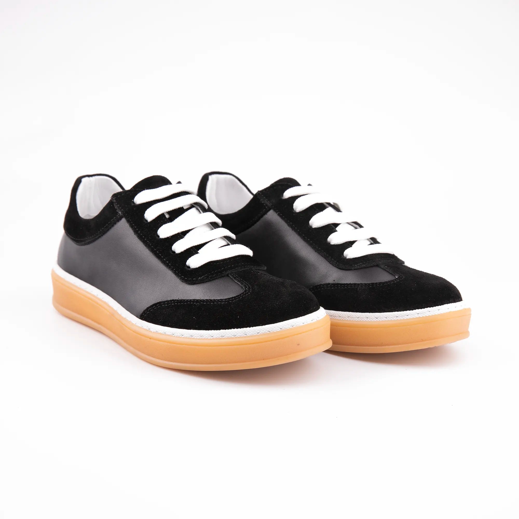 A pair of MrCalvano Redondo women's casual sneakers, featuring black matte leather panels, black suede overlays on the toe, heel, and eyestay, optic white laces, a thick natural gum rubber sole, and a thin white stripe separating the upper from the sole. Shot on a white background, showcasing the textural contrast.