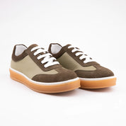 A pair of MrCalvano Redondo Beach green leather women sneakers, featuring a sage green smooth leather upper with chocolate brown suede overlays, white laces, white midsole trim, and a translucent amber gum sole, positioned for an e-commerce product display.