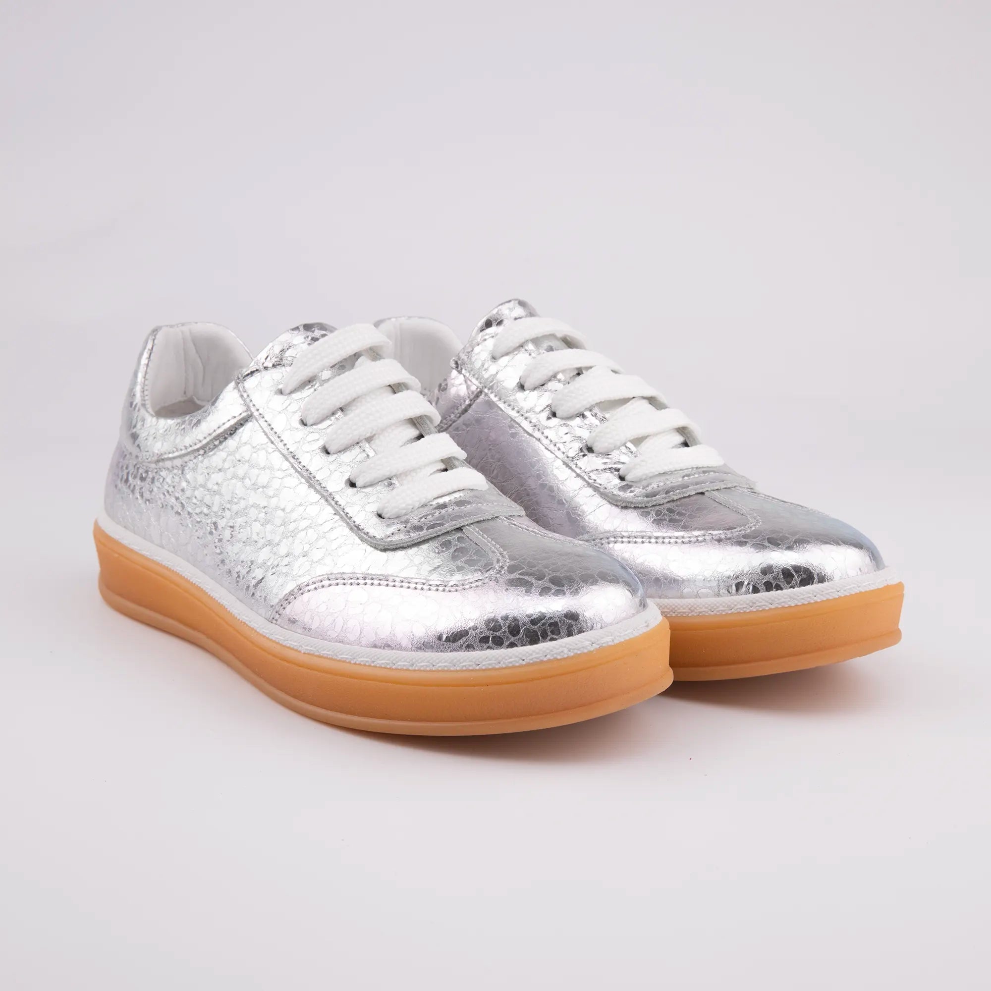 A pair of MrCalvano Redondo silver leather women's sneakers, showcasing the unique cracked metallic texture, optic white laces, and light tan gum sole, photographed on a clean white background for the United State market.