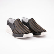 A pair of MrCalvano Solana Black Leather Women's Slip-On Shoes, showcasing the perforated black and bronze leather upper, the distinctive off-white sculpted sole, and the contrasting white stitching at the toe. Shot on a white background, emphasizing the modern design and materials ideal for wear in the United State.