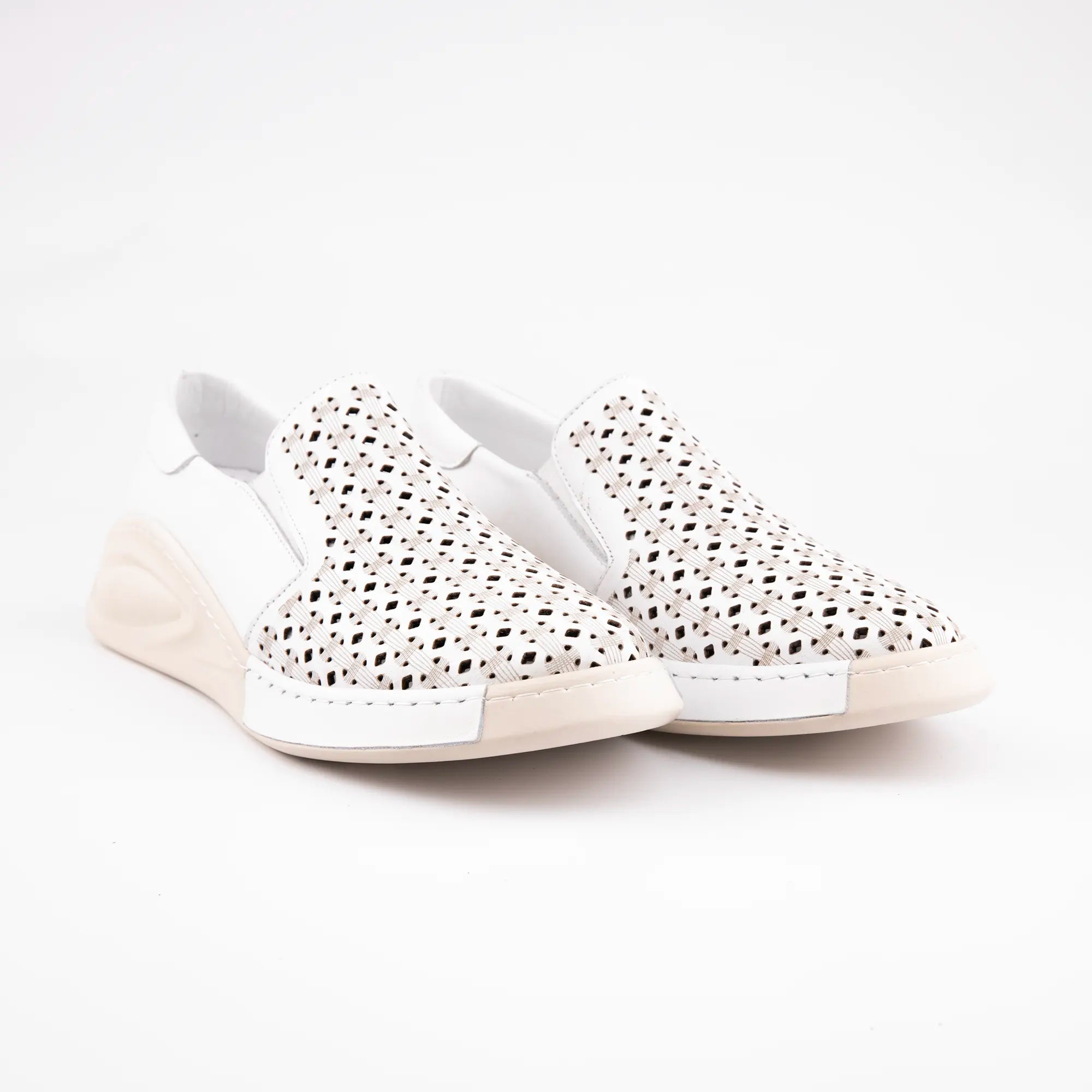 A pair of pristine white women's slip-on shoes, crafted from smooth and perforated leather, with a distinctive creamy off-white sole. The perforations form a diamond-weave pattern across the toe and vamp, allowing for airflow. The sole has a gentle wedge shape at the heel, integrated into its contoured design. Photographed against a minimalist background, highlighting the clean lines and material contrast.
