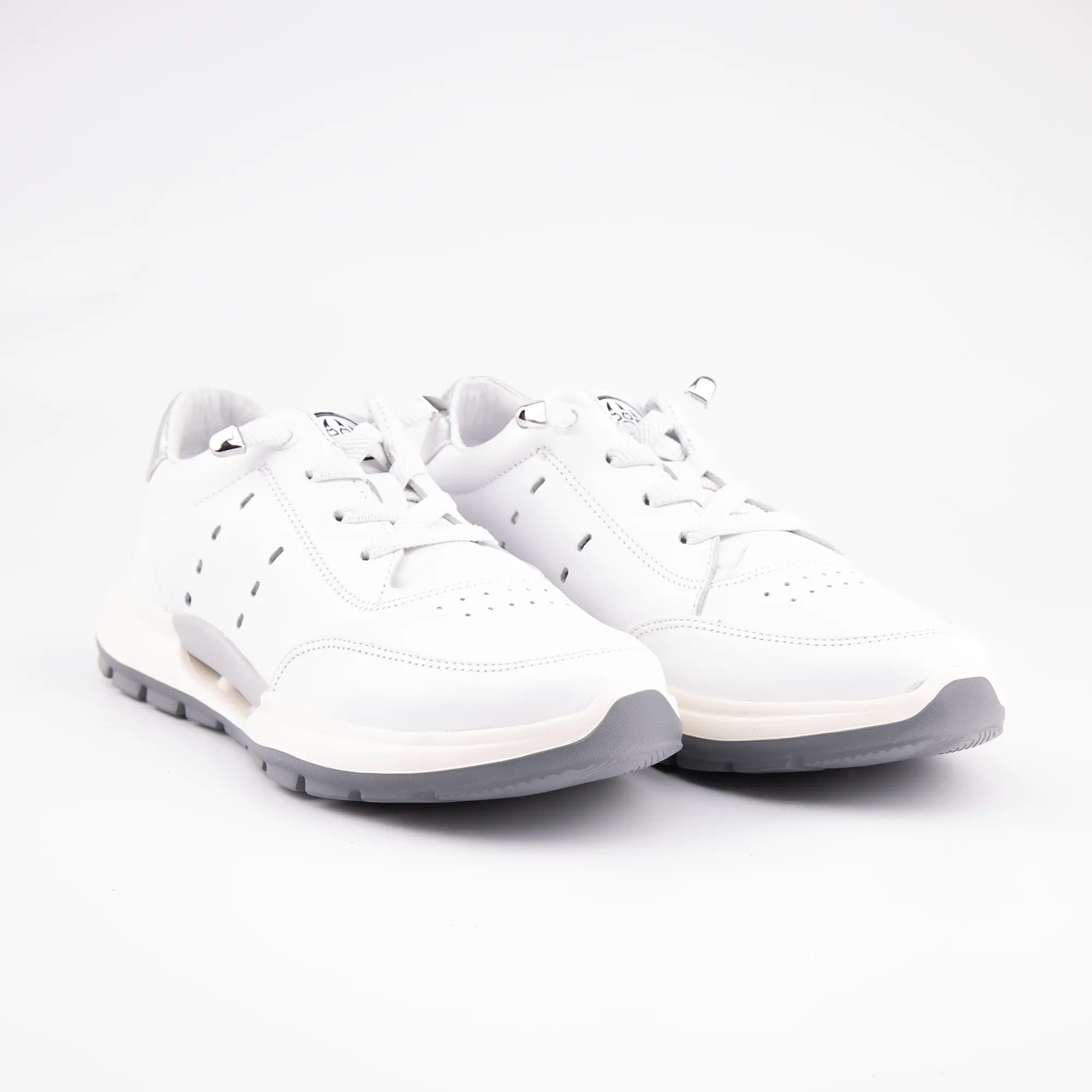 A pair of MrCalvano Venice Beach white leather women's sneakers, featuring a smooth white leather upper, a multi-layered off-white and light slate grey sole with subtle tread, and a metallic silver heel tab, presented on a minimalist white background.
